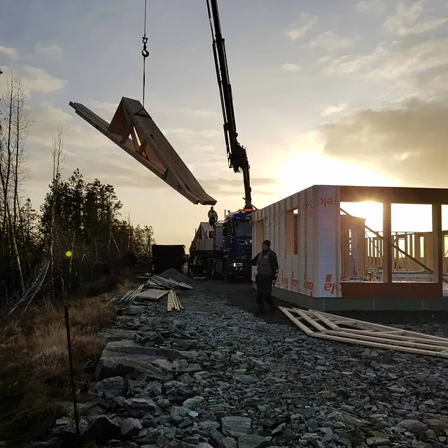 Kran løfter takstol ved husbygging i solnedgang