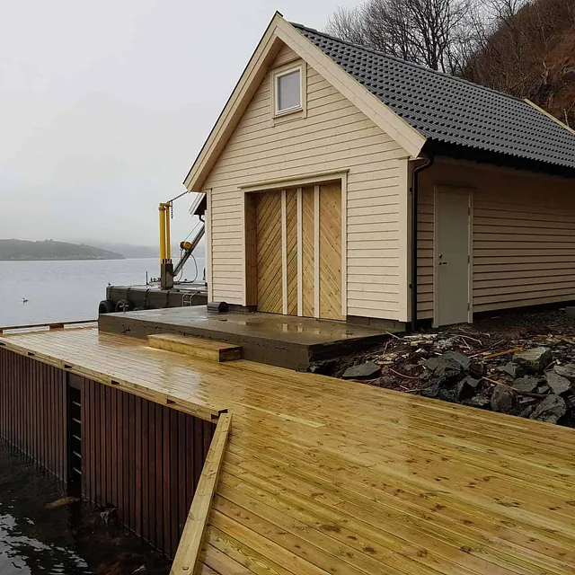 Ferdig båthus med brygge ved vannet i overskyet vær